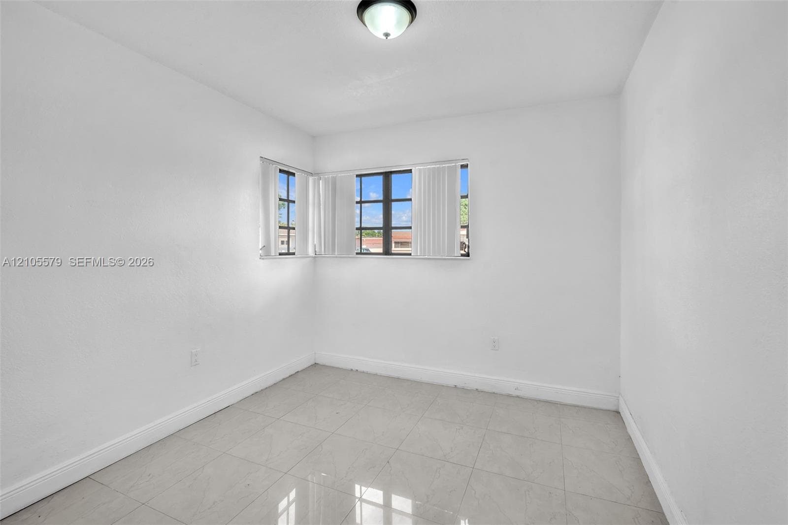 Neutral interior space featuring polished tile flooring, smooth white walls, corner-positioned multi-pane windows, and a flush-mount ceiling fixture