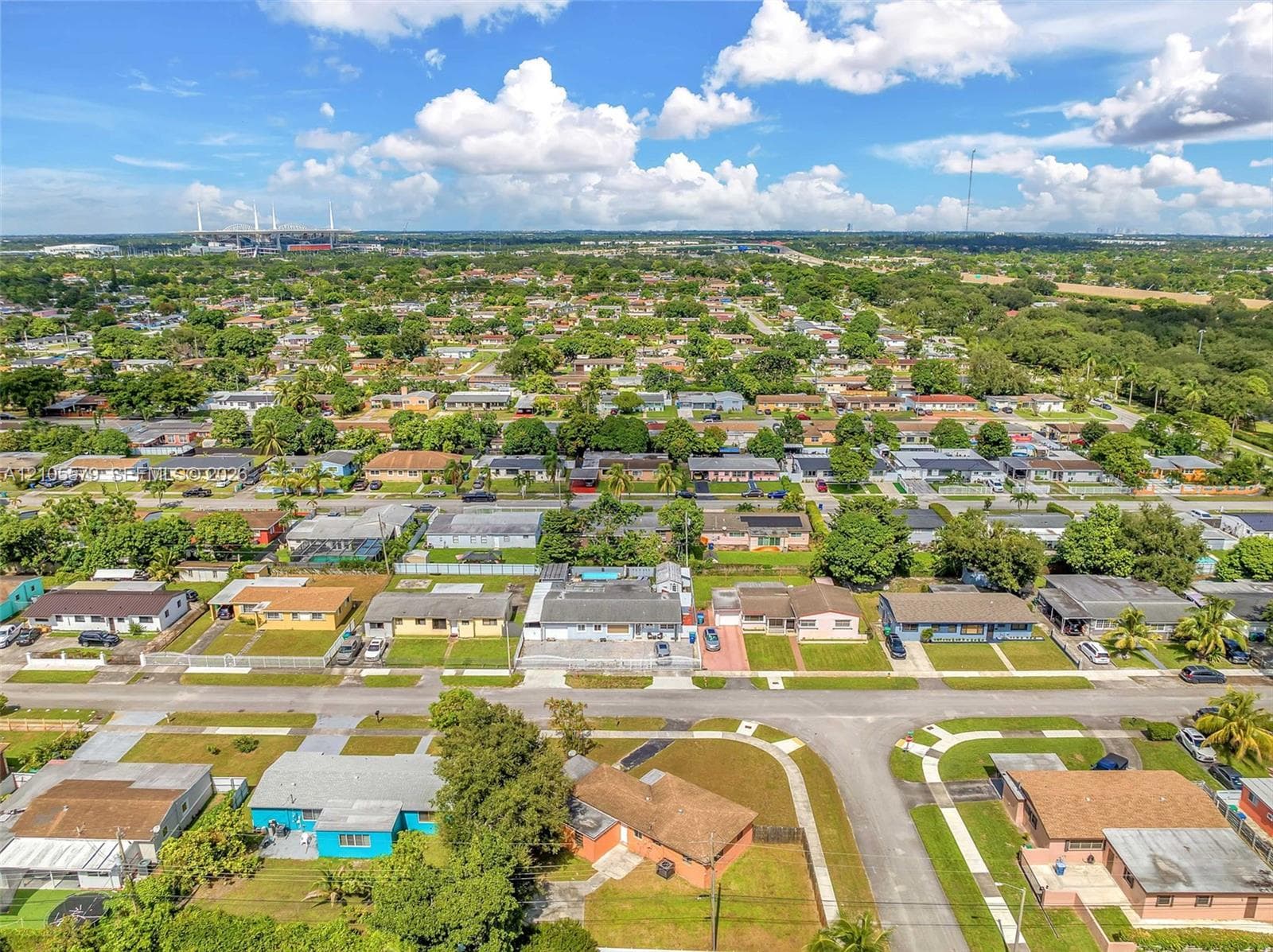 Aerial perspective of the residential property featuring a paved driveway, a multi-car garage, an enclosed rear patio, and mature landscaping
