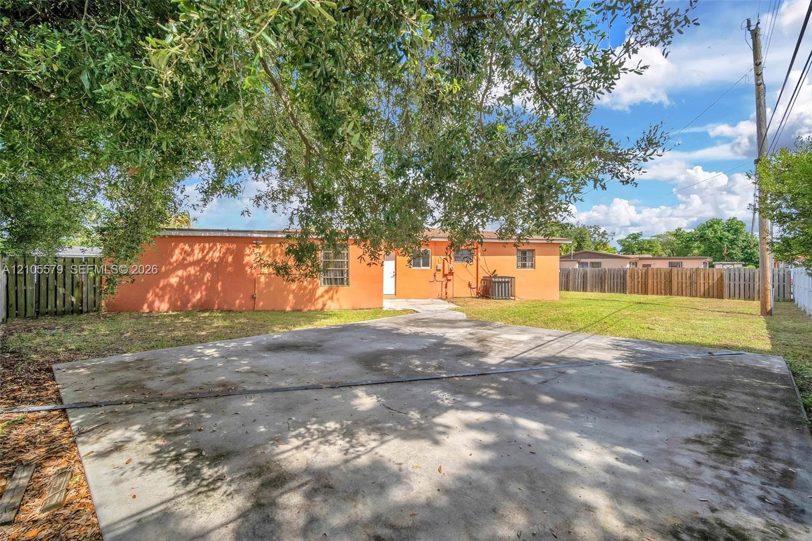 Stucco exterior featuring a concrete driveway, fenced perimeter, and mature canopy trees
