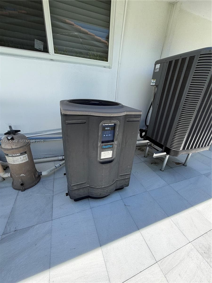 Exterior mechanical systems featuring a heat pump and additional outdoor unit, situated on a tiled surface