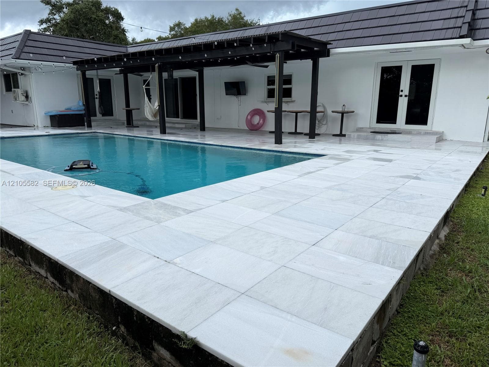 Outdoor swimming pool with a black-framed pergola, white tiled pool deck, and white exterior stucco finish