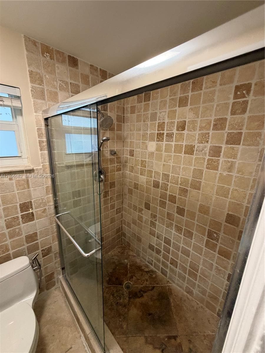 Enclosed shower with tiled walls and floor, featuring a glass sliding door and a shower head with an attached sprayer