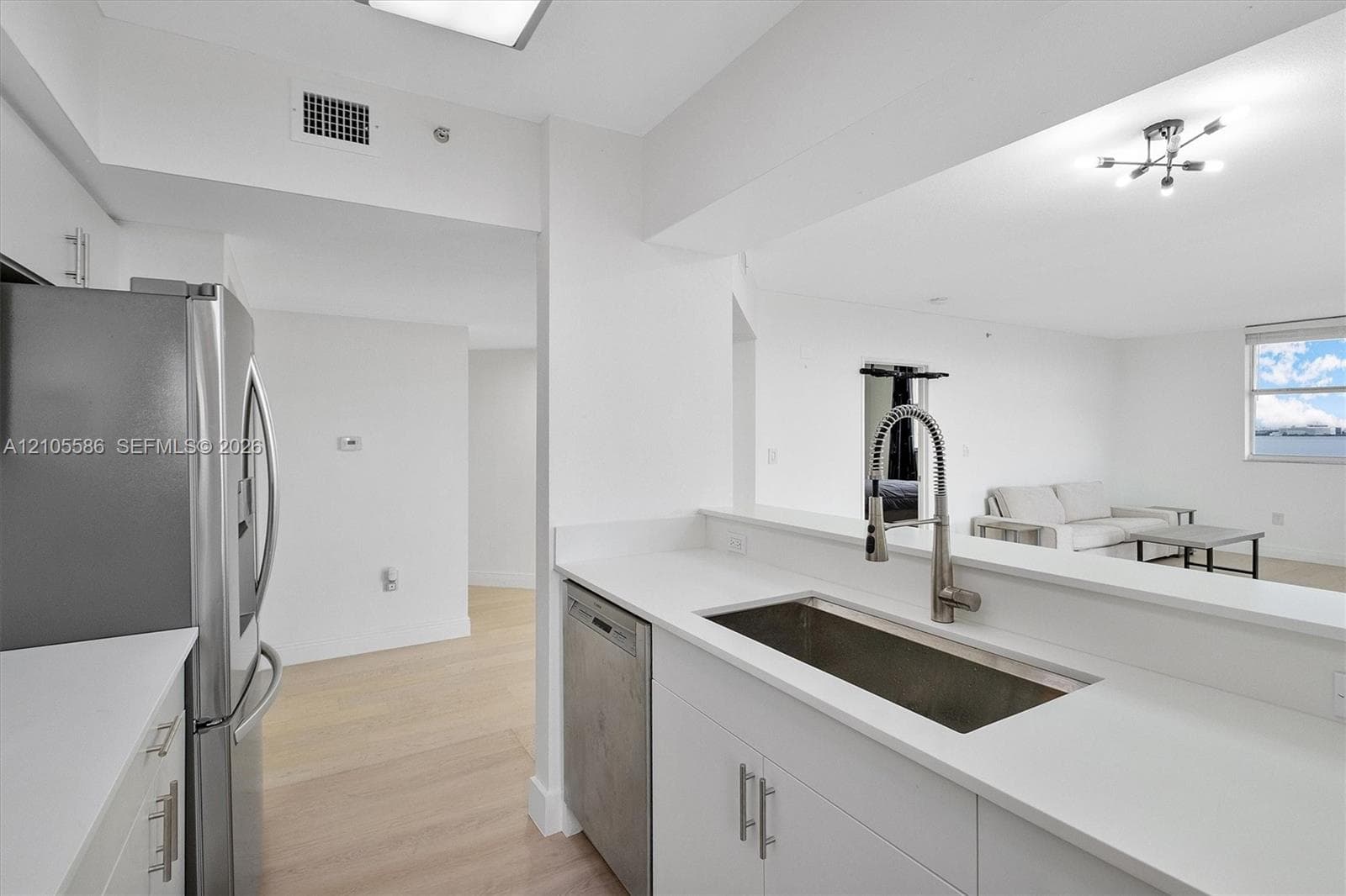 Contemporary kitchen featuring white cabinetry, light countertops, stainless steel appliances, and wood-finish flooring