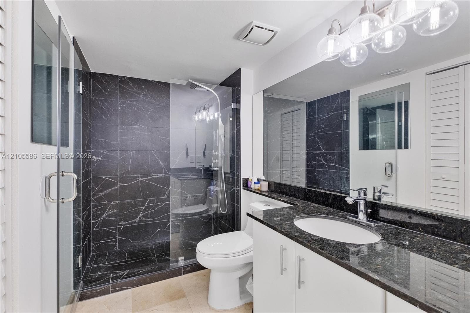 Full-height black stone-look shower surround, glass-enclosed shower, white vanity with stone-look countertop, integrated sink, and large wall-mounted mirror