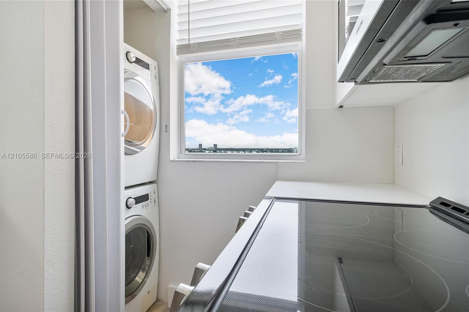 Integrated stacked washer and dryer, white countertops, built-in cooktop, and window with exterior scenery