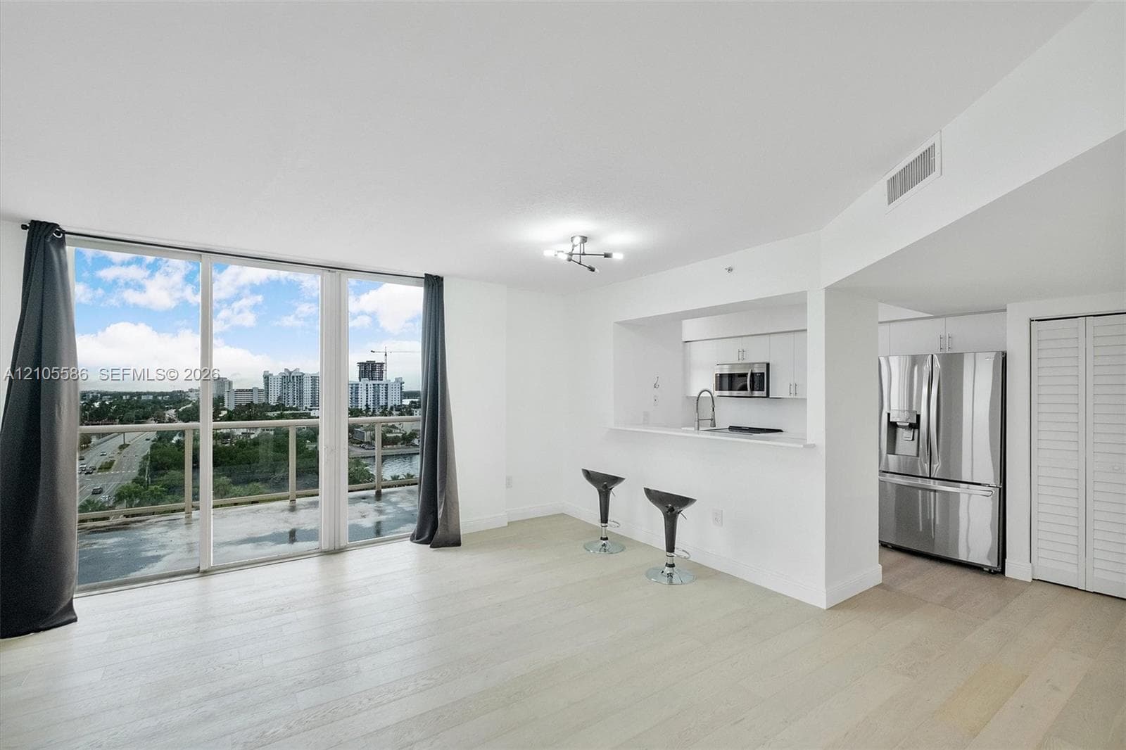 Spacious living area featuring light wood-finish flooring, floor-to-ceiling sliding glass doors, and a contemporary light fixture