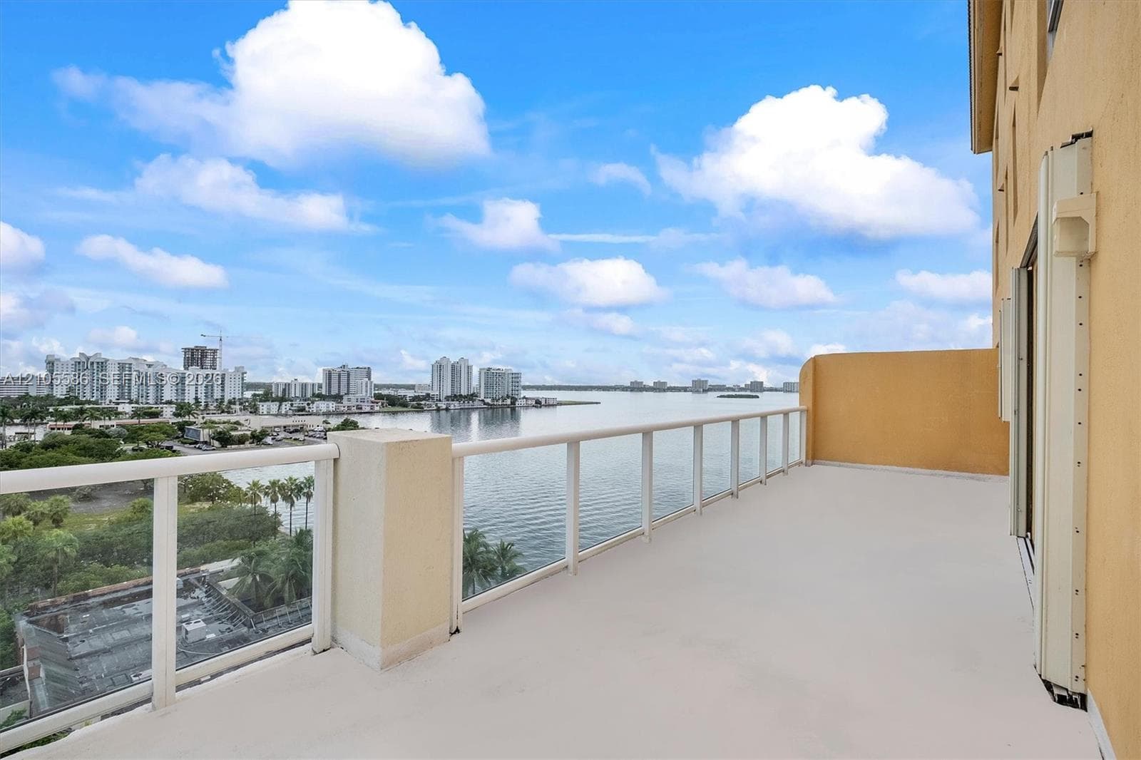 Expansive balcony with glass panel railings, overlooking a body of water and city skyline