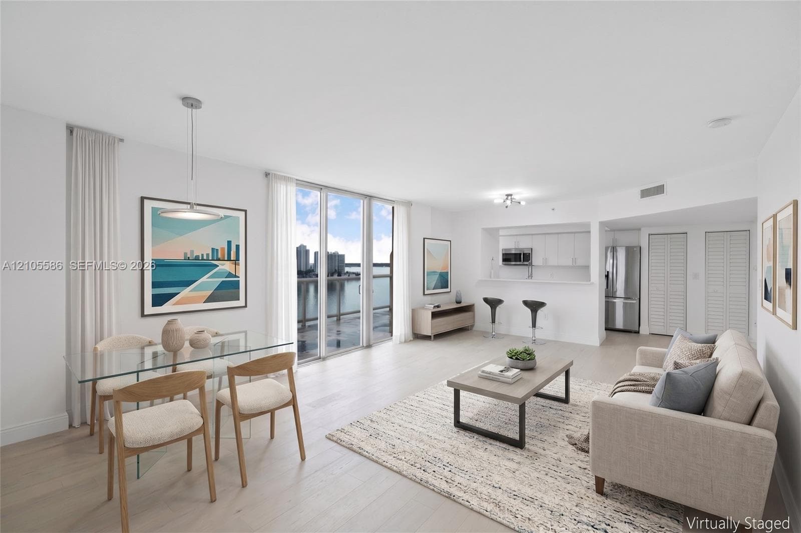 Open-concept living space with light wood-finish flooring, floor-to-ceiling sliding glass doors, a kitchen featuring stainless steel appliances, and a breakfast bar