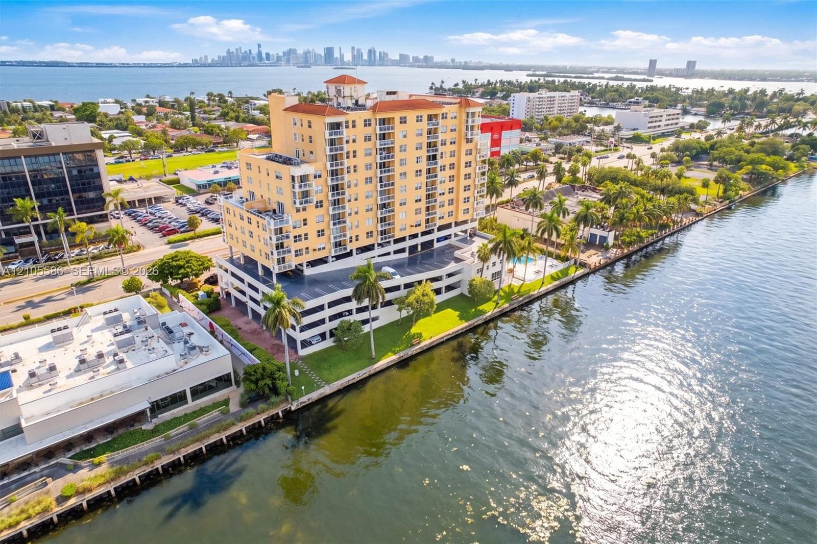 Waterfront high-rise building with multi-level parking structure, swimming pool, and established landscaping