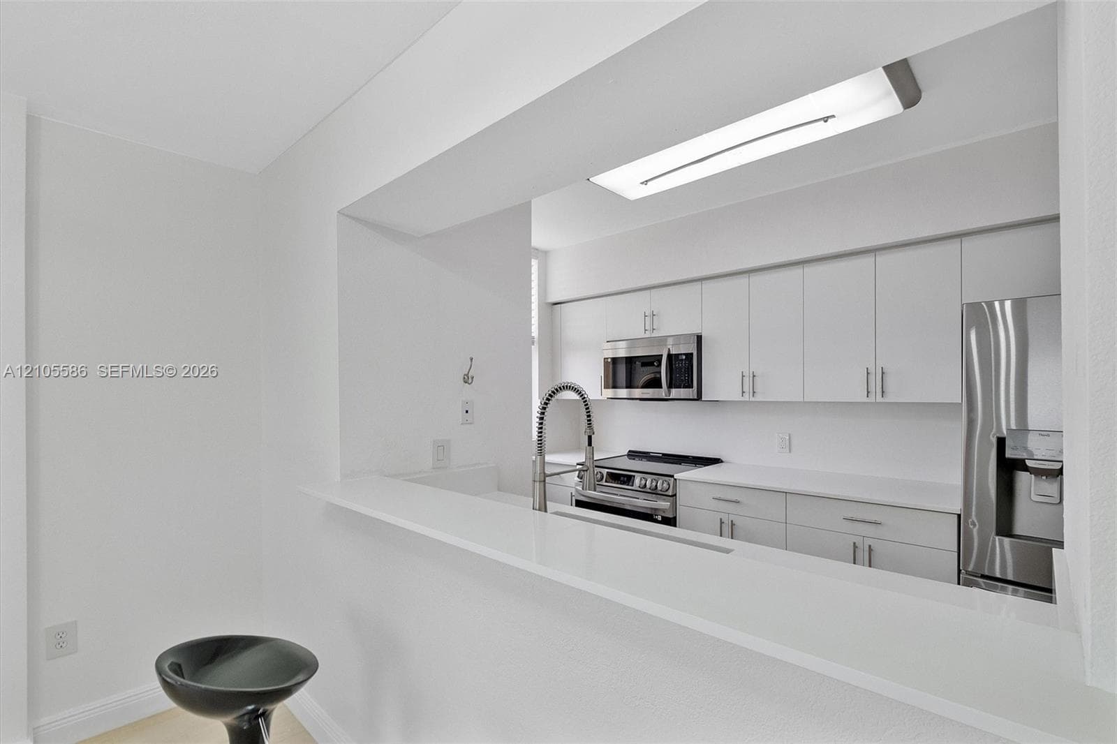 Kitchen pass-through featuring white cabinetry, stainless steel appliances, and a solid surface countertop