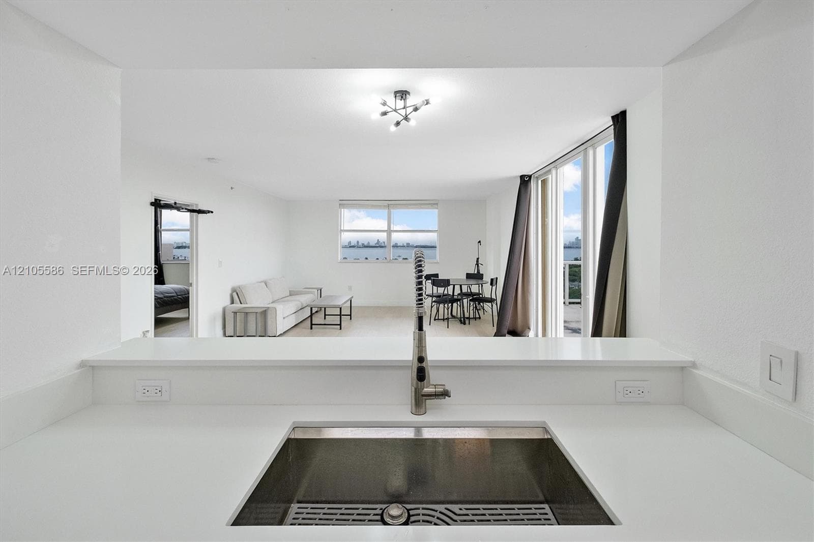 Sleek kitchen featuring a stainless steel sink with a high-arch faucet, white countertops, and a pass-through opening to the living area