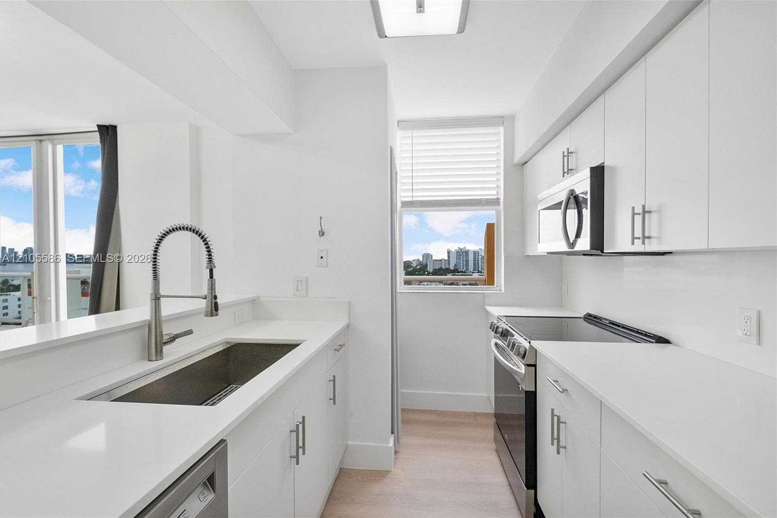 Contemporary kitchen featuring white cabinetry, light countertops, stainless steel appliances, and wood-finish flooring