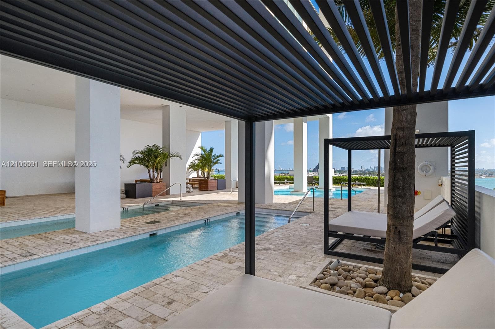 Outdoor amenity area with a louvered pergola, multiple pools, and extensive stone tile decking