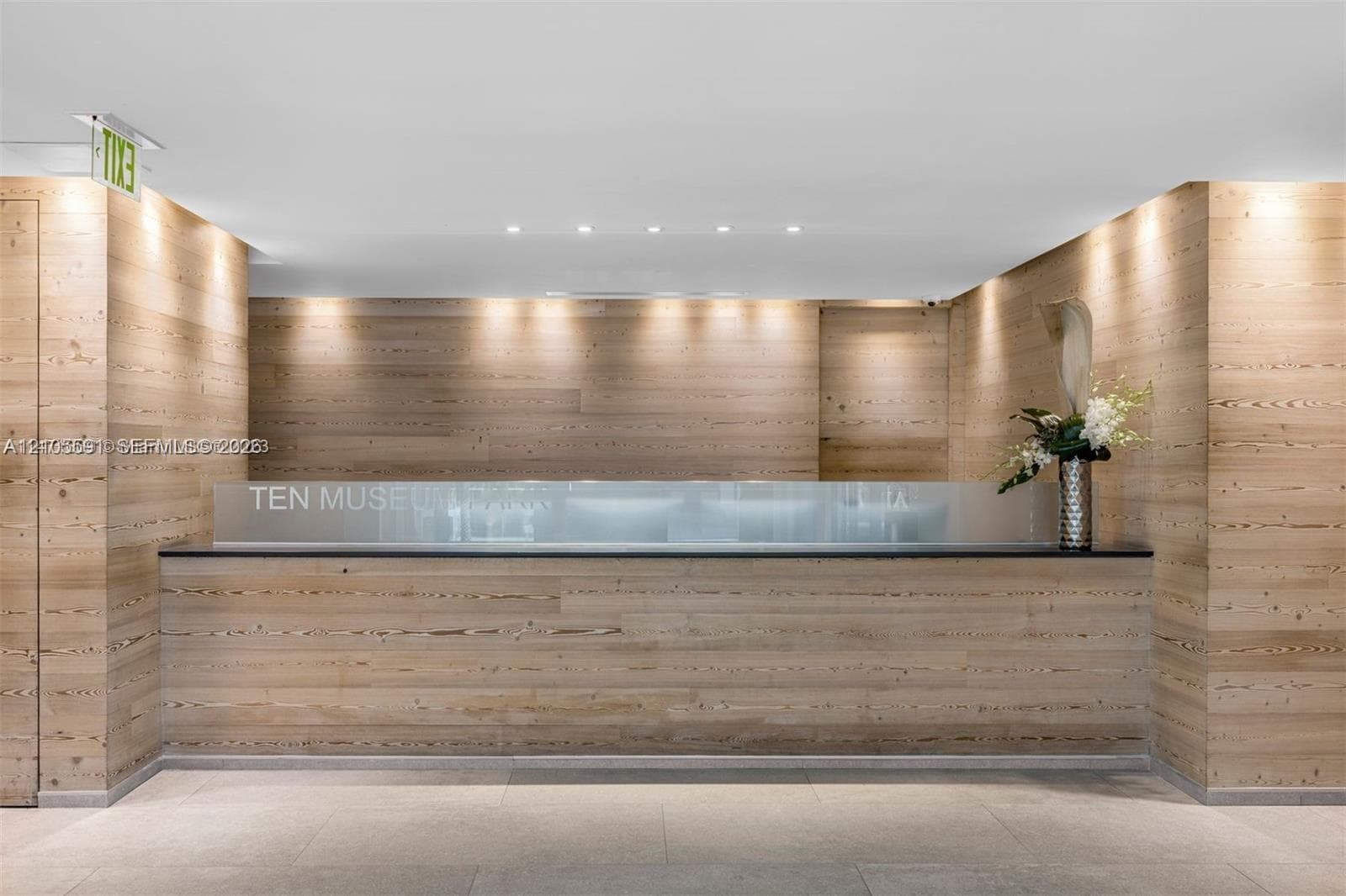 Wood-paneled reception area featuring a frosted glass counter, recessed ceiling lighting, and overhead accent lighting