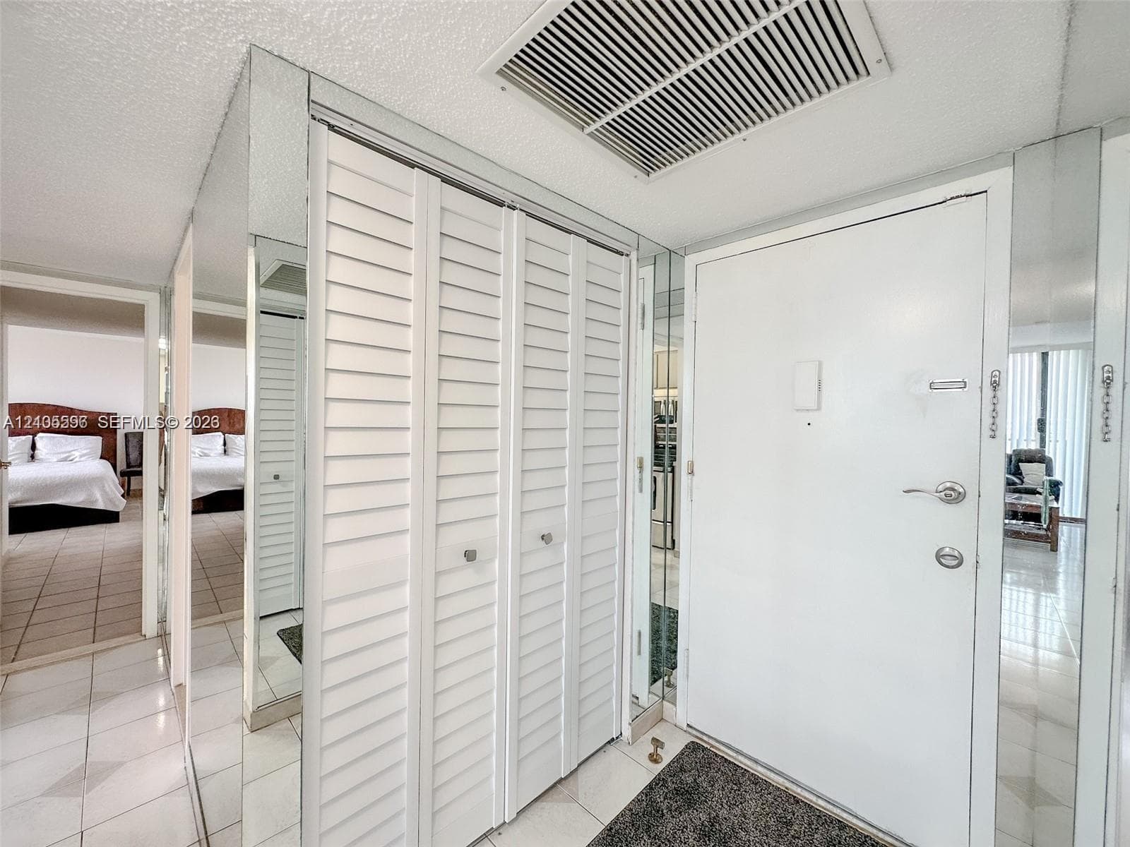 Entryway featuring floor-to-ceiling mirror panels, white louvered closet doors, and tile flooring