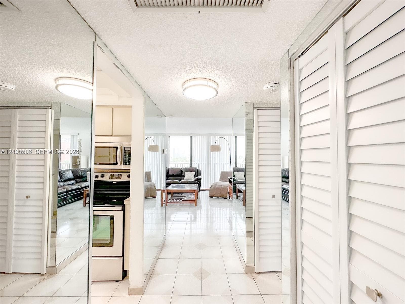 Full-length mirrored wall panels, white louvered closet doors, polished tile flooring, and flush-mount ceiling lighting