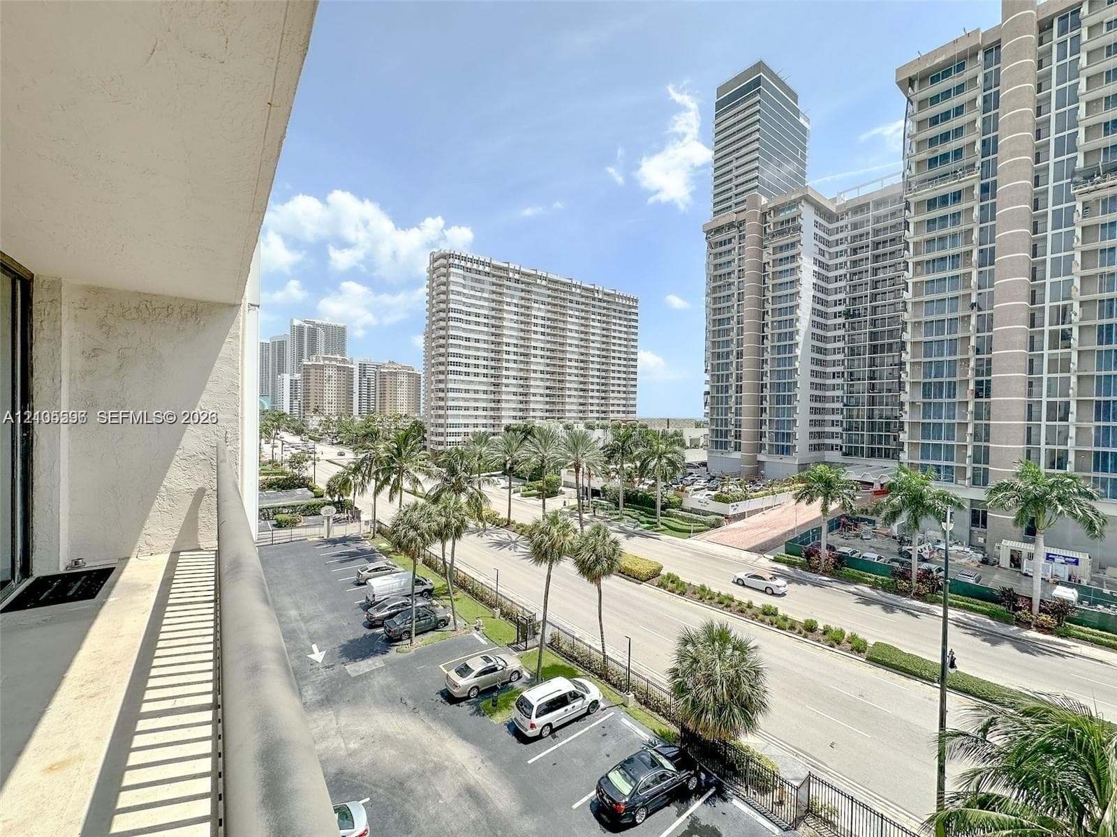 Elevated balcony featuring a metal railing and concrete flooring with an urban perspective of multi-story architecture and mature palm trees