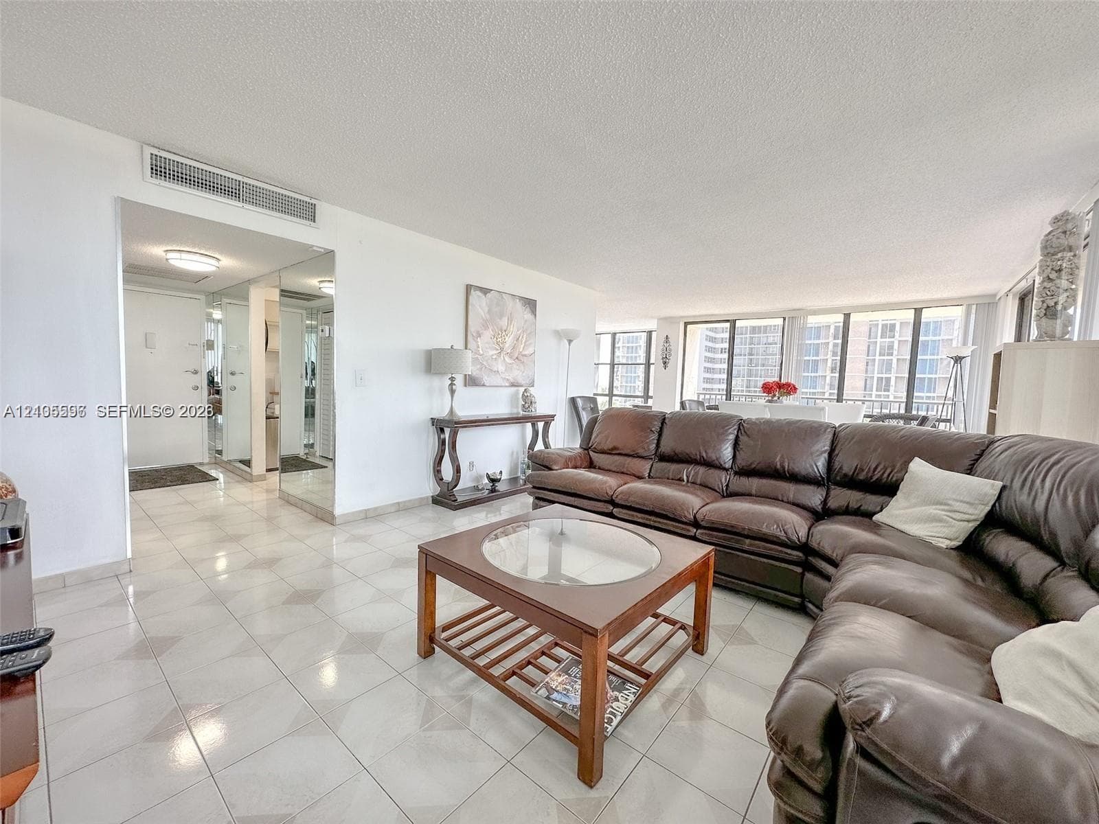 Living area featuring light-toned tile flooring, floor-to-ceiling windows, and mirrored wall accents
