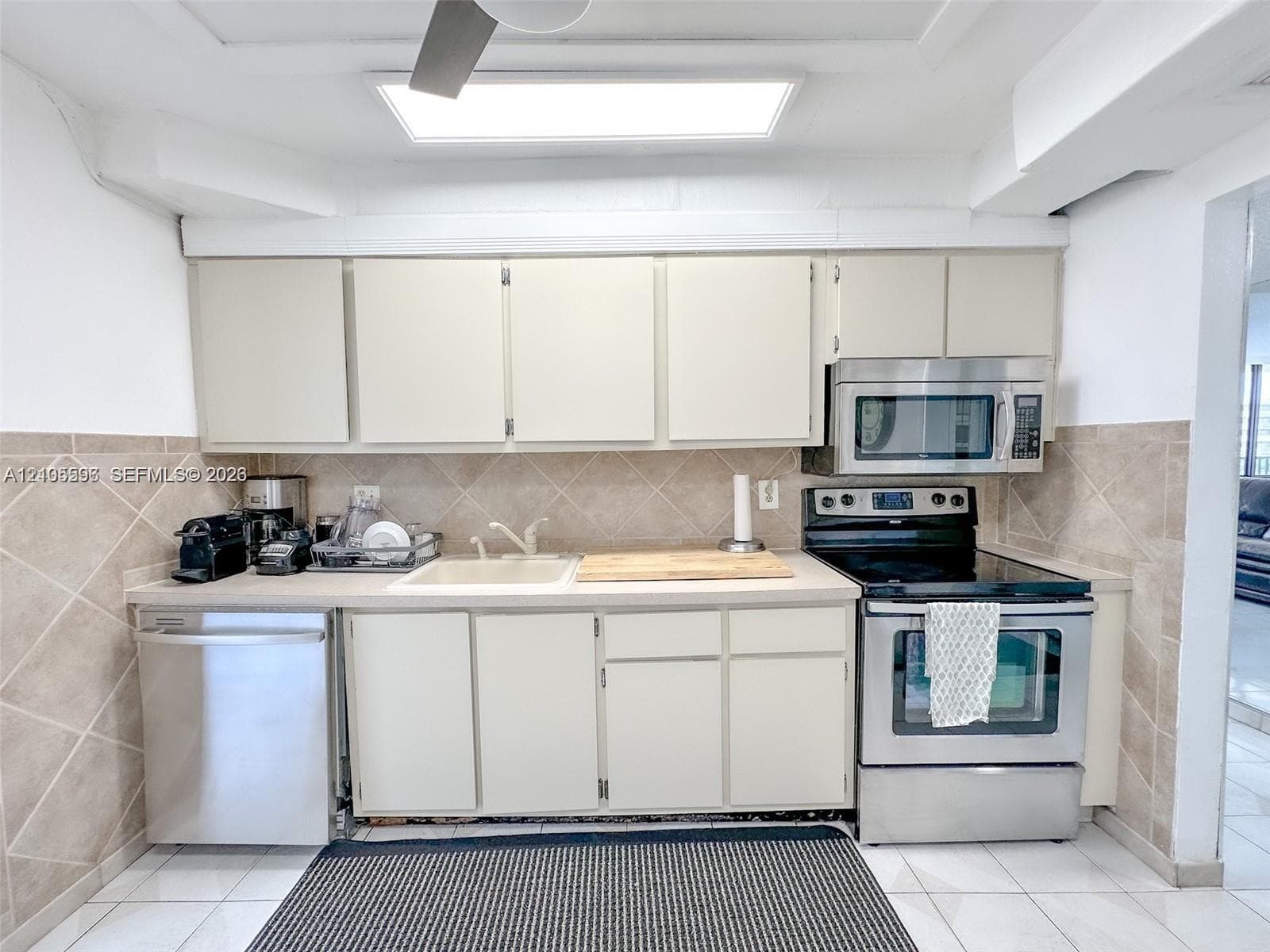Kitchen featuring flat-panel cabinetry, stainless steel appliances, stone-finish backsplash, built-in recessed ceiling lighting, and tile flooring