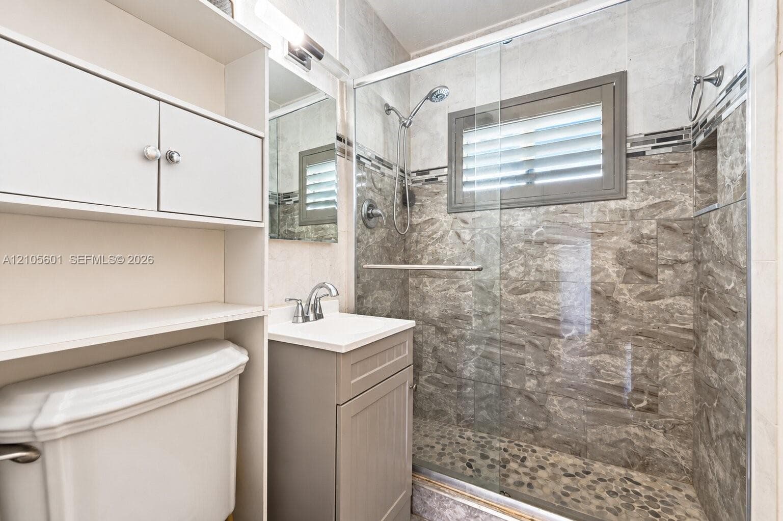 Glass-enclosed shower with pebble-finish flooring and stone-look tile surround