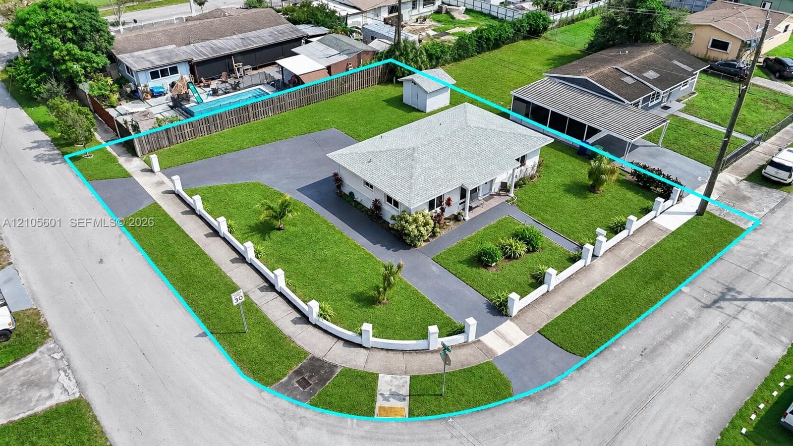 Corner lot with a white single-story residence, a detached shed, a paved driveway, a gated front yard, and a covered carport