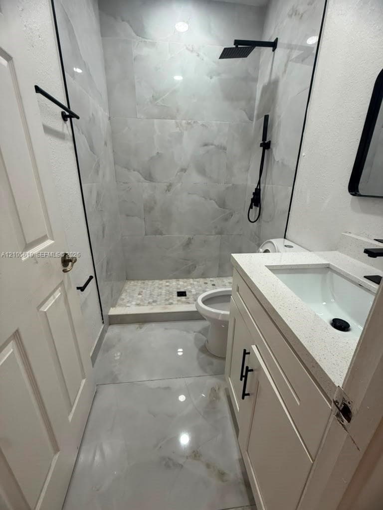 Bathroom featuring large-format tile flooring, a walk-in shower with floor-to-ceiling tile surround and a pebble-tiled base, a vanity with a quartz countertop, and matte black hardware