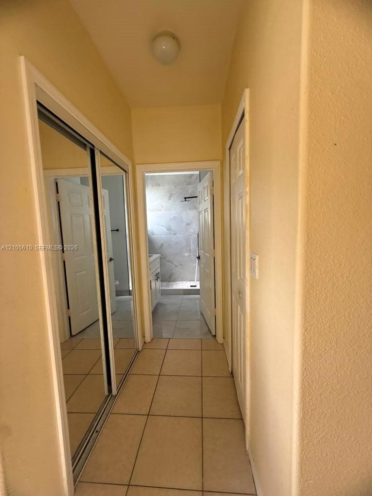 Hallway featuring large-format ceramic tile flooring, floor-to-ceiling mirrored sliding closet doors, and solid-core six-panel interior doors