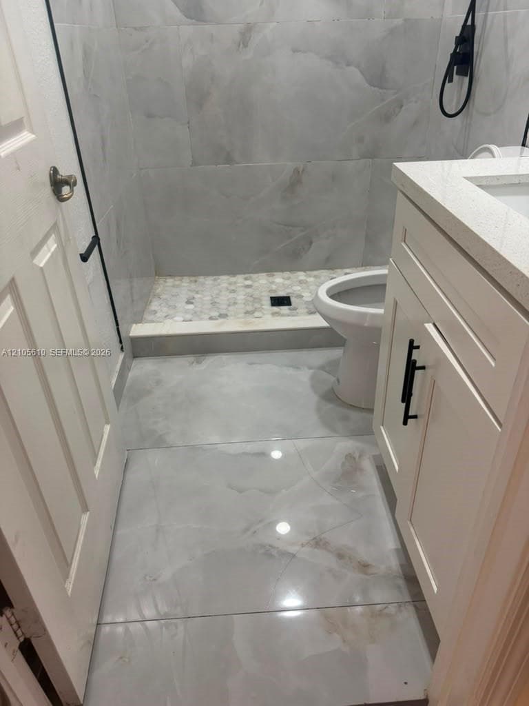 Bathroom featuring large-format porcelain tile flooring, a shower with floor-to-ceiling tile surround and a stone-pebble shower floor, quartz vanity countertop, and matte black cabinet hardware