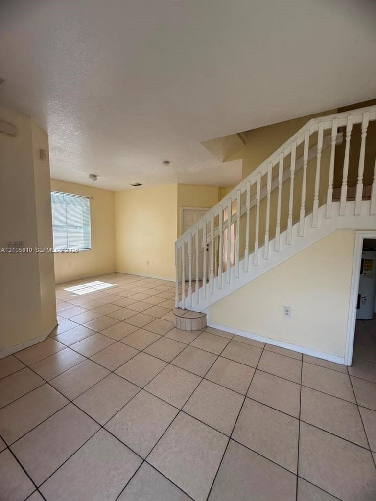 Open-concept floor plan featuring tile flooring throughout and a white wooden staircase with balustrade railings