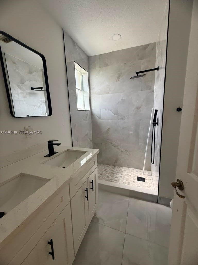 Double vanity with stone-composite countertop, matte black fixtures, walk-in shower with large-format tile surround, and tile flooring
