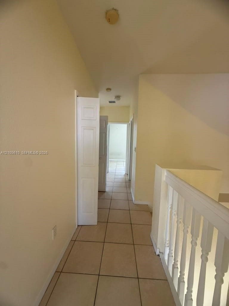 Hallway featuring neutral tile flooring, white paneled interior doors, and a staircase balustrade with a wooden handrail