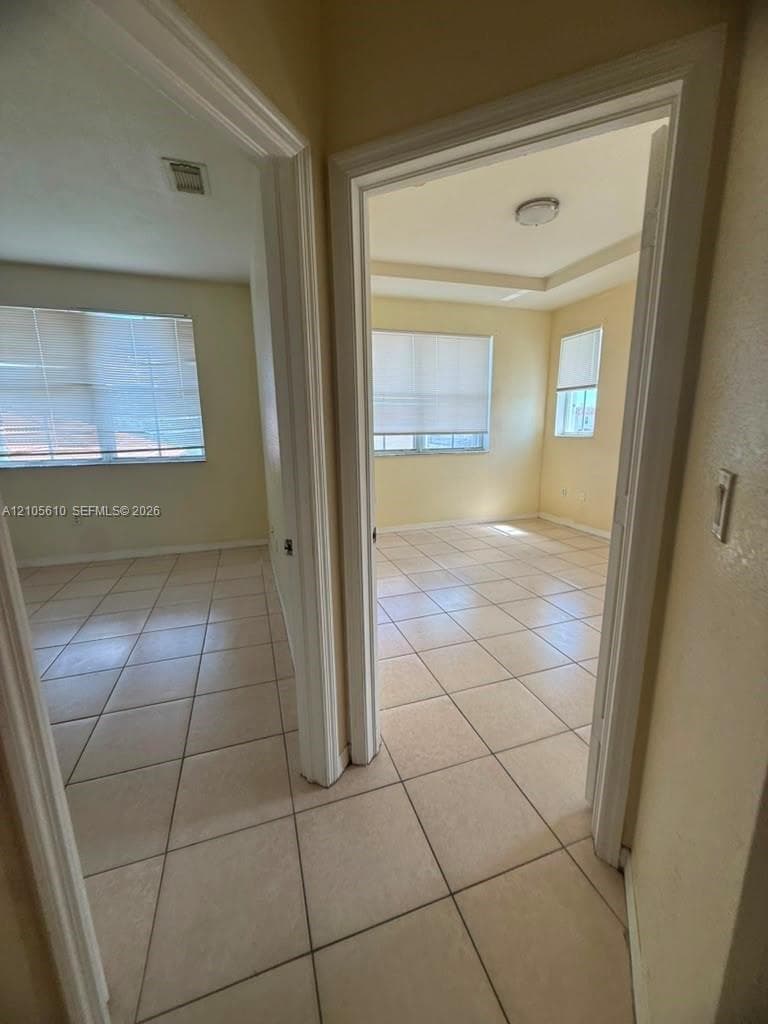 Tile flooring, multiple windows with blinds, recessed ceiling tray, and flush-mount lighting fixtures