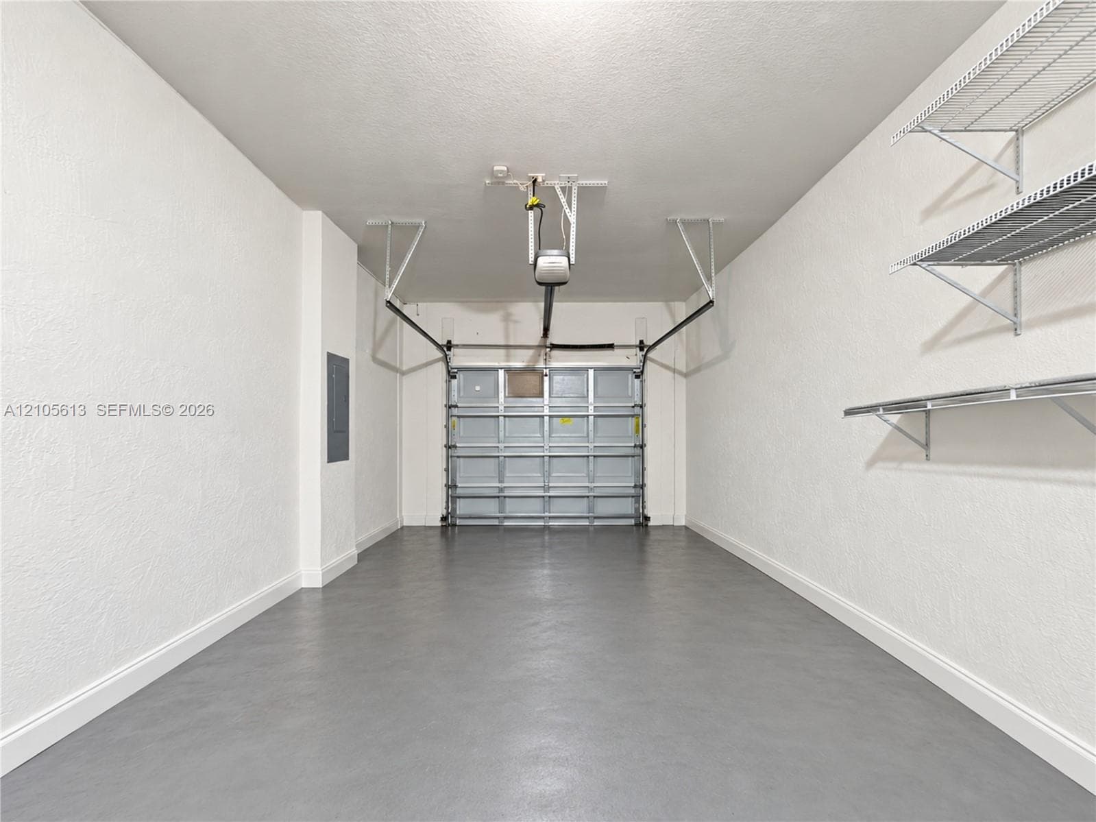 Garage space featuring a smooth painted floor finish, textured walls, overhead door opener, and mounted wire shelving units
