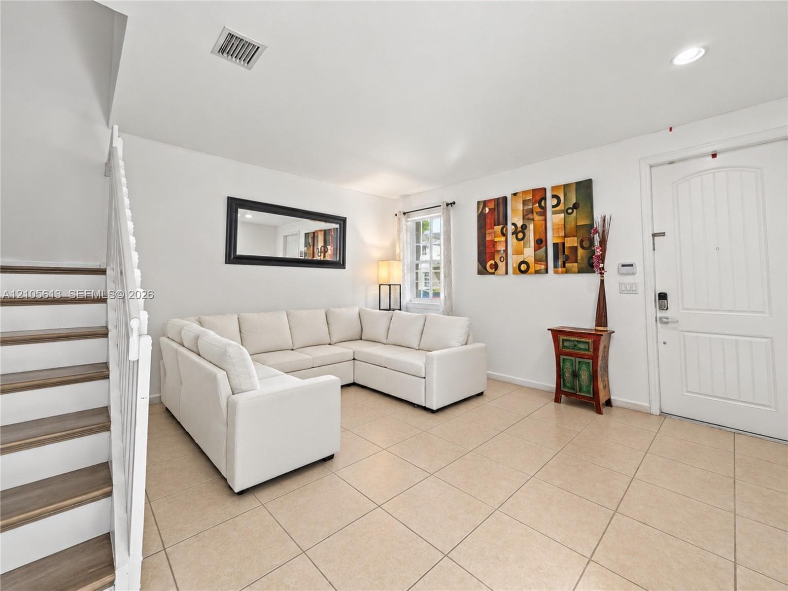 Living area featuring large-format neutral tile flooring, recessed lighting, and a white staircase with wood-finish treads and white balusters
