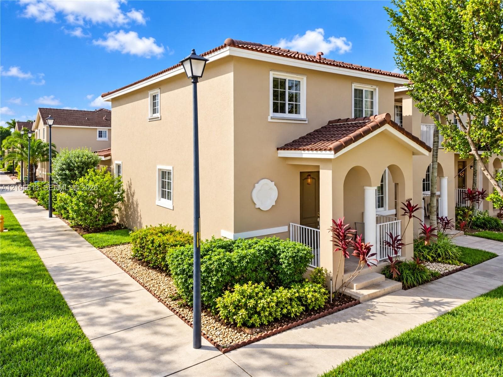 Stucco exterior featuring a covered entryway with arched openings, tiled roof, white-trimmed windows, and decorative architectural medallion