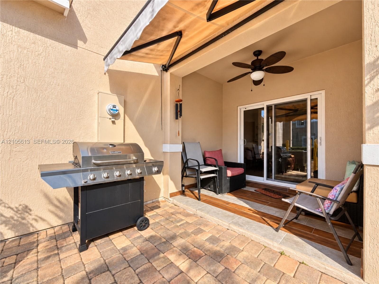 Covered patio featuring a paver surface, retractable awning, ceiling fan, and sliding glass door