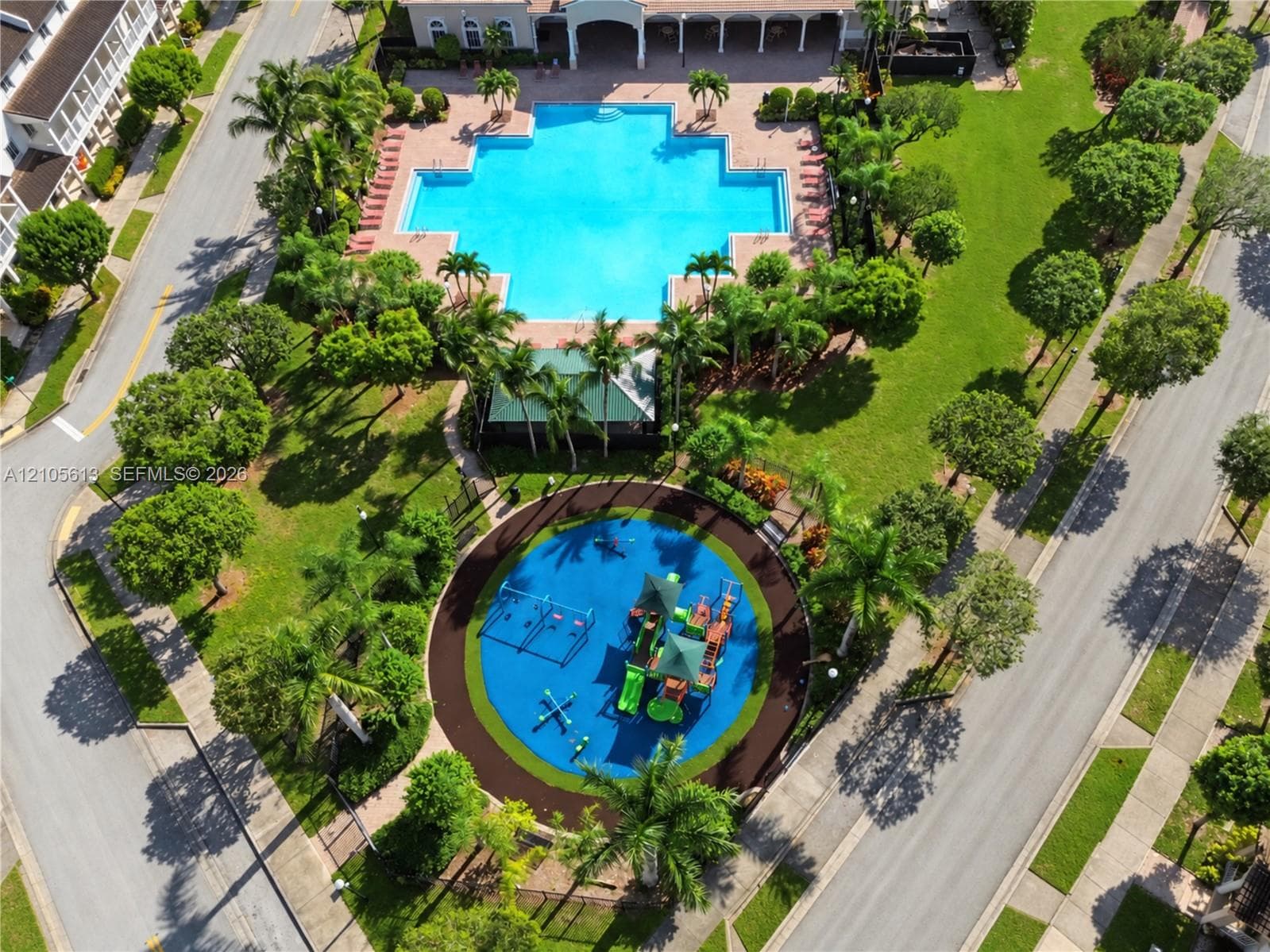 Aerial perspective featuring a communal swimming pool, a playground with specialized rubberized surfacing, paved walking paths, and mature landscaping