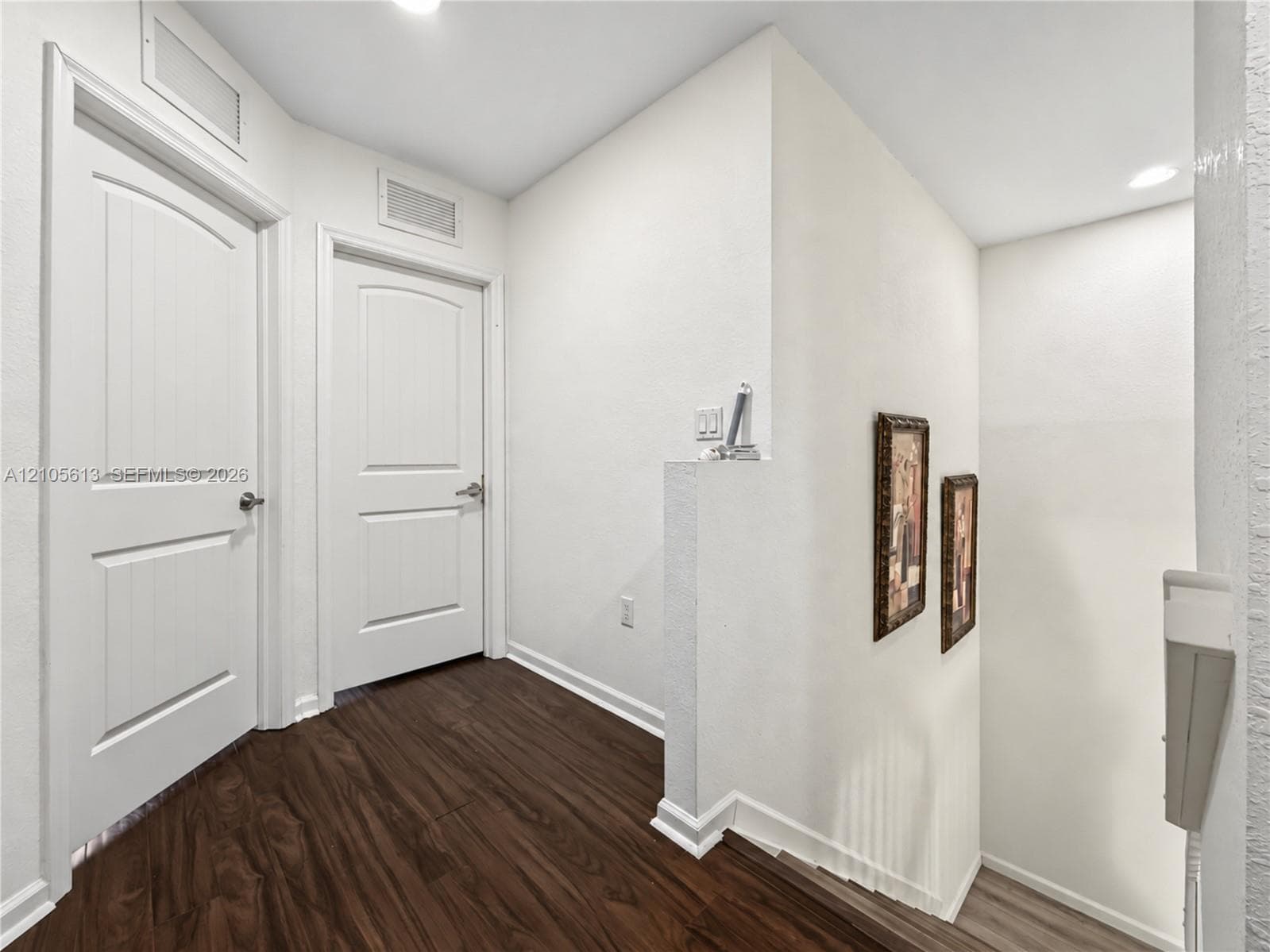 Interior hall featuring wood-finish flooring, white walls, and two-panel interior doors with satin-finish hardware