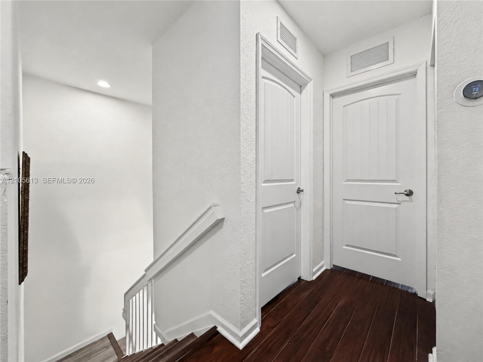 Hallway featuring wood-finish flooring, two solid-core arched two-panel doors, and a smart thermostat