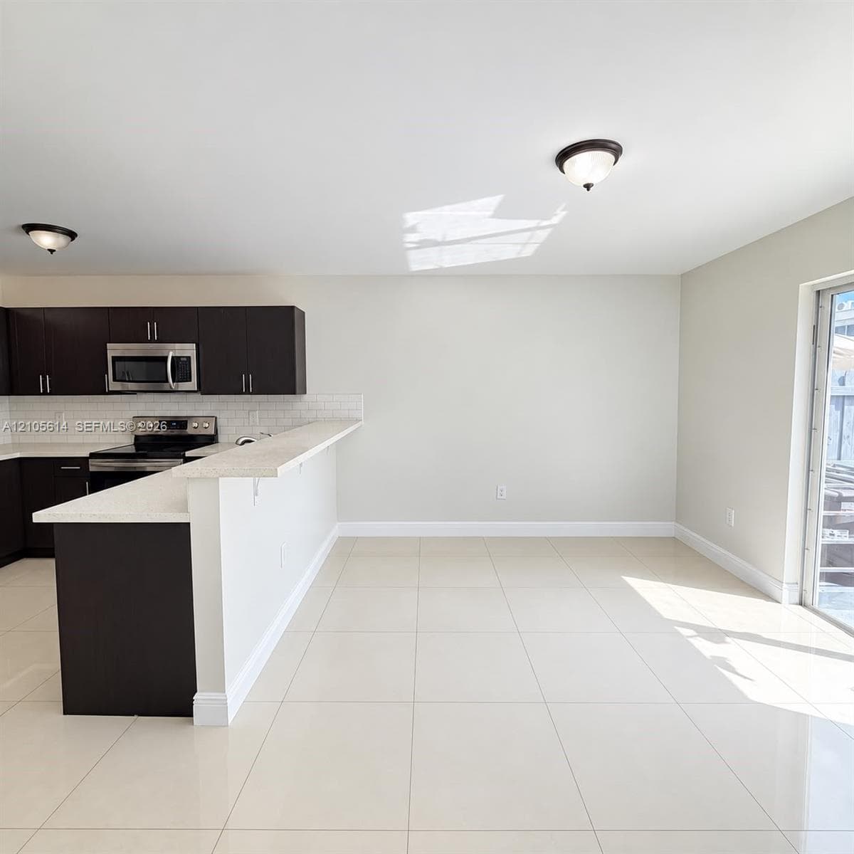 Kitchen featuring dark-finish cabinetry, stone-composite countertops, breakfast bar, white tile backsplash, and ceramic floor tiling