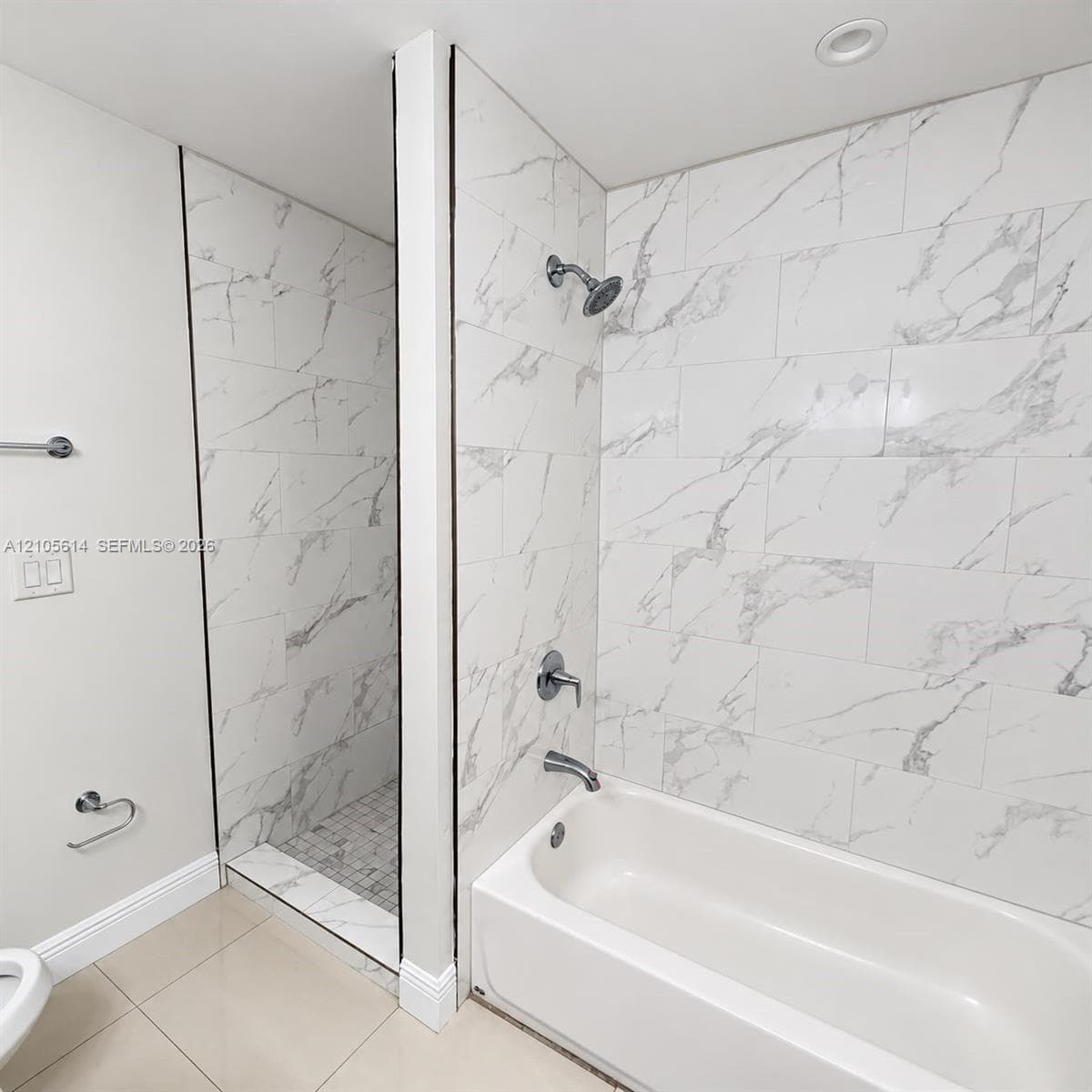 Shower and bathtub combination featuring large-format white stone-finish tile surround with gray veining, chrome plumbing fixtures, and a recessed tiled shower floor