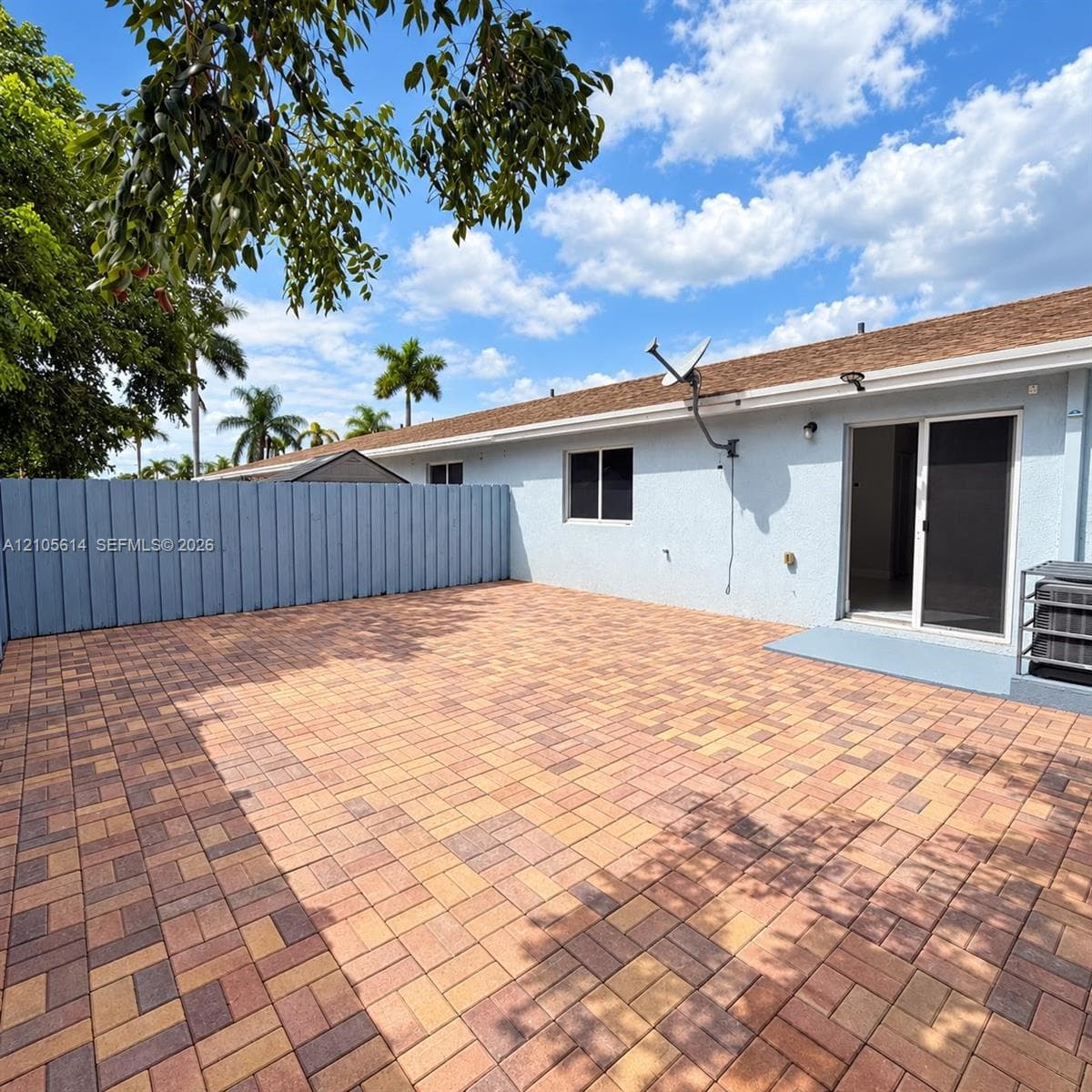 Backyard area featuring a multi-tone paver patio, a solid wood-panel perimeter fence, and sliding glass exterior doors