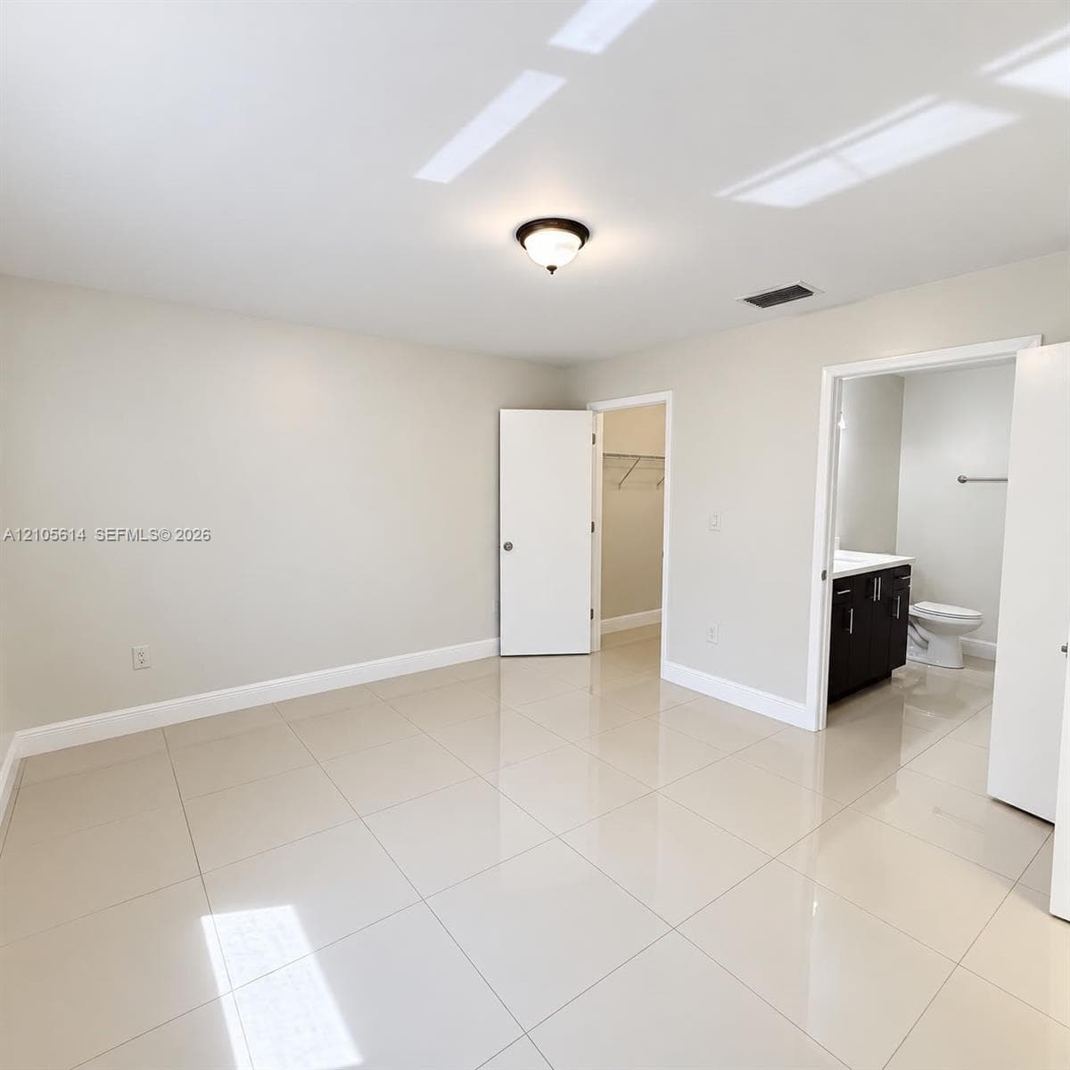Neutral-toned interior featuring polished tile flooring, flush-mount ceiling lighting, built-in closet, and bathroom cabinetry with a solid-surface countertop