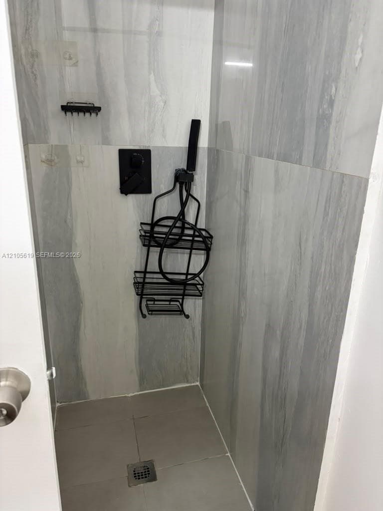 Walk-in shower featuring large-format gray veined tile, matte black wall-mounted faucet, and square floor drain