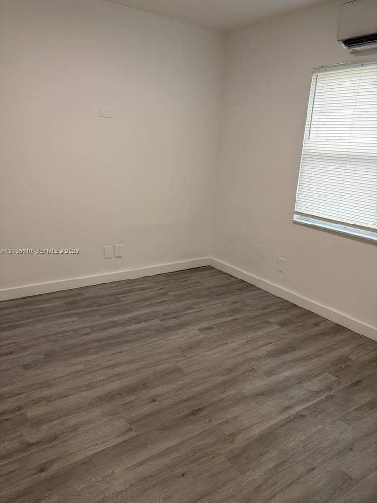 Room featuring wood-finish flooring, neutral wall paint, and a wall-mounted ductless climate control unit