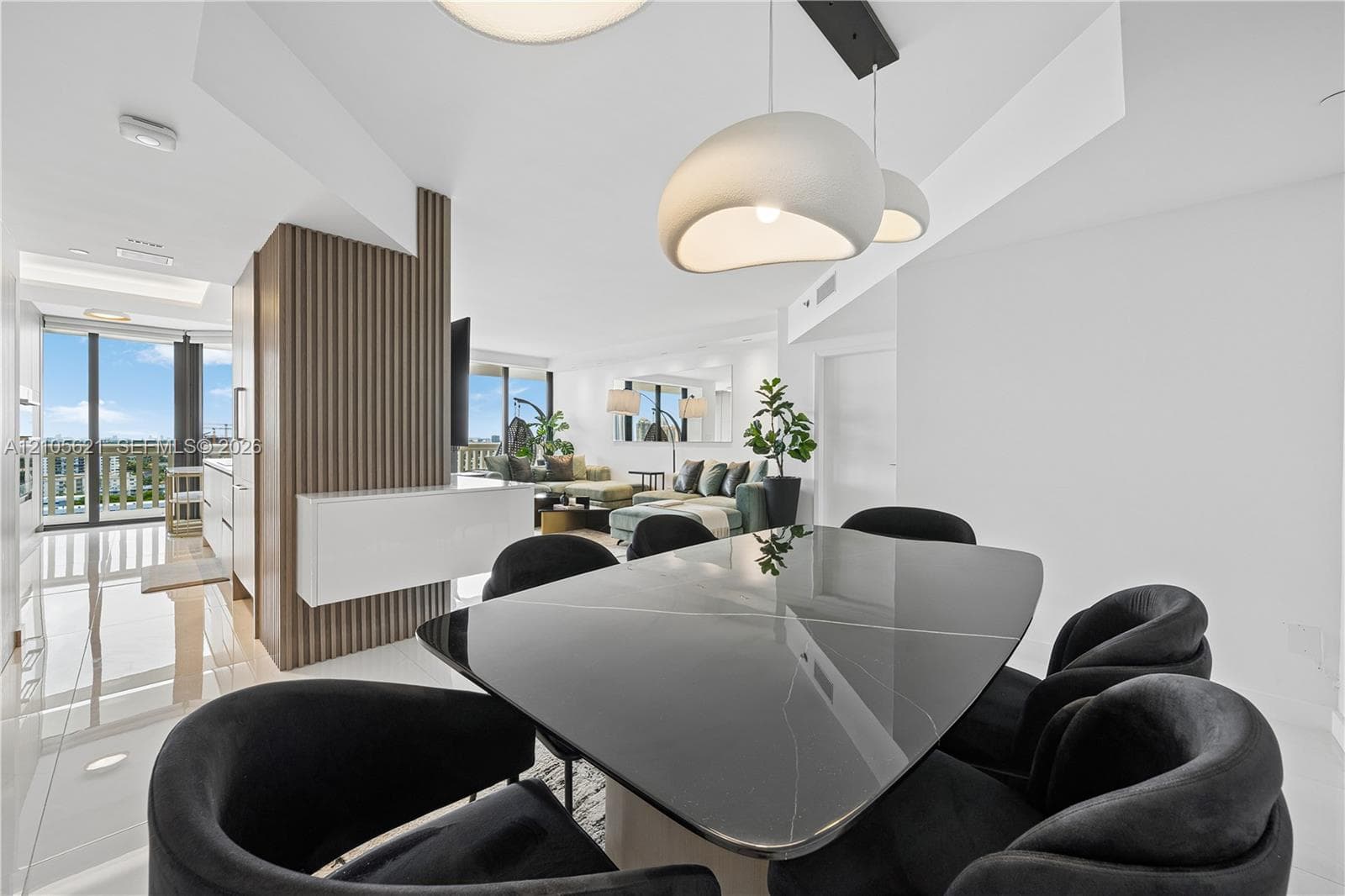 Open-concept interior featuring vertical slat wood-finish wall paneling, oversized sculptural pendant lighting, floor-to-ceiling glass sliding doors, and polished tile flooring