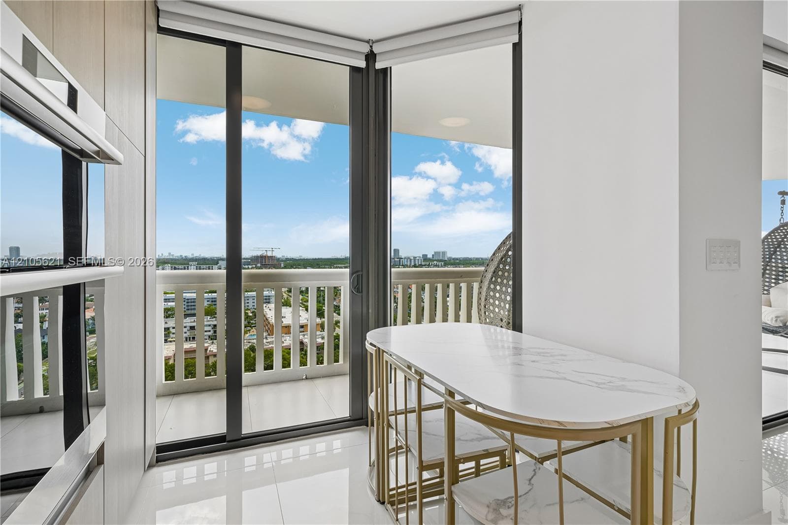 Floor-to-ceiling glass sliding doors, private balcony with decorative railing, built-in dual wall ovens, and large-format porcelain tile flooring