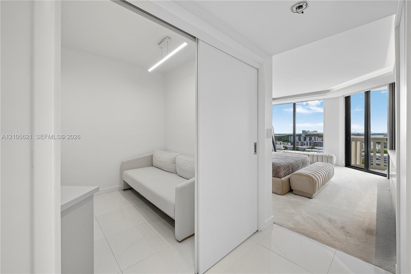 Interior space featuring white tile flooring, a sliding white privacy door, and floor-to-ceiling windows with natural lighting