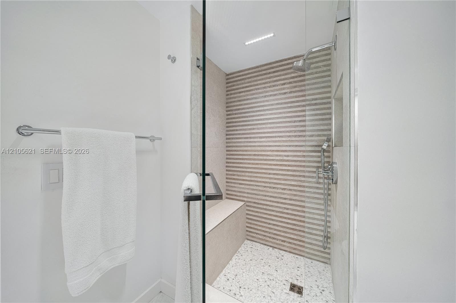 Walk-in shower featuring a glass enclosure, textured horizontal tile accent wall, built-in tile bench, terrazzo-style floor tile, and polished chrome dual-function shower head