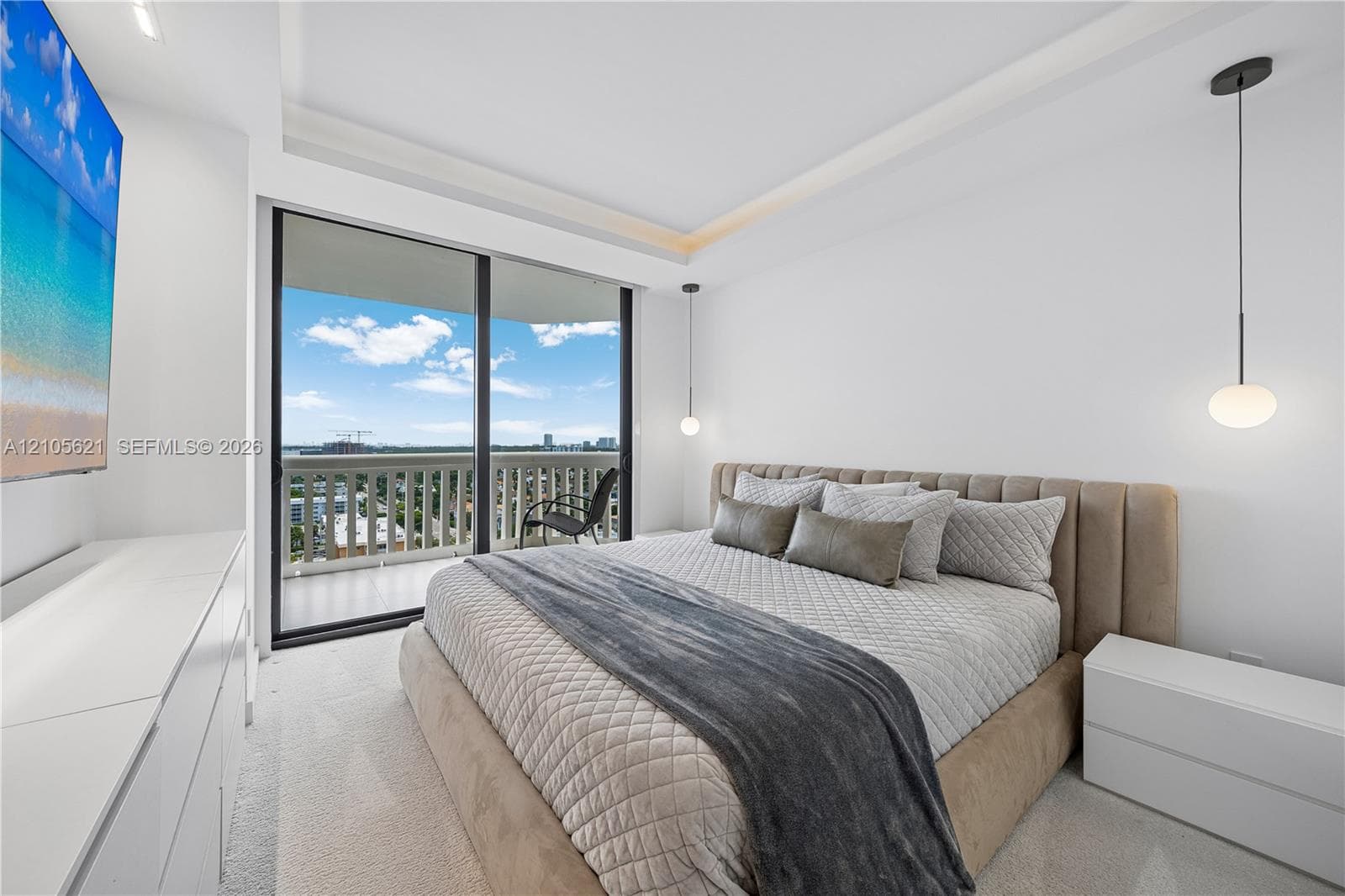 Tray ceiling with recessed lighting, floor-to-ceiling glass sliding doors, private balcony, and dual modern pendant light fixtures